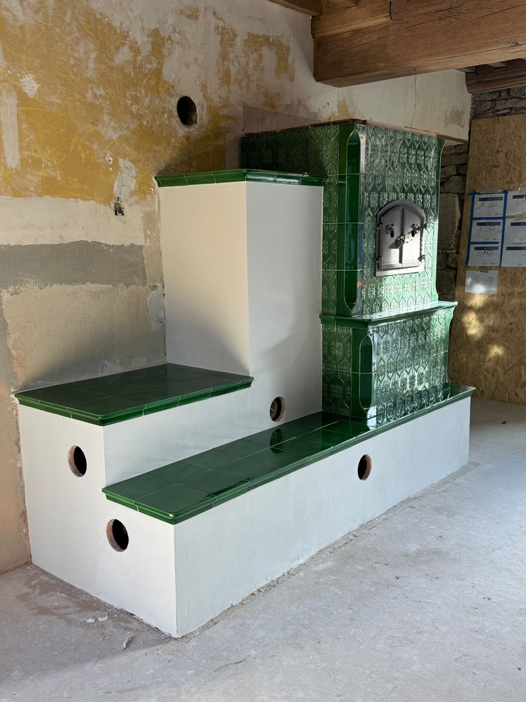 Two green-tiled heated benches at right angles around the tiled heater, white rendered base