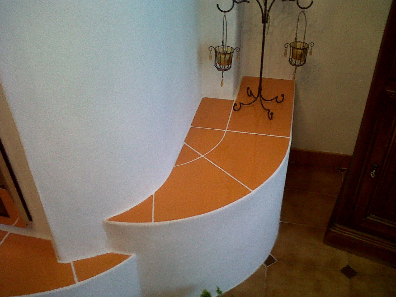 Site-built heated bench in a quarter circle, rendered white, seat tiled with terracotta tiles laid in a fan pattern
