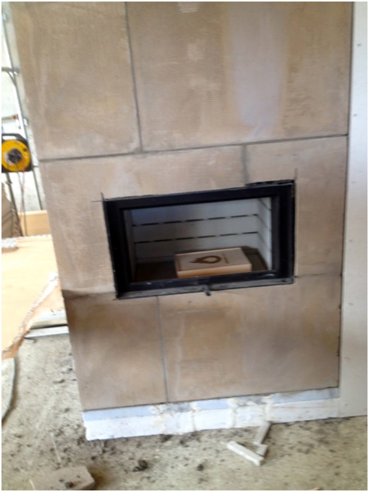 Masonry heater clad in large beige slabs laid in staggered bond, horizontal firebox set flush with the masonry