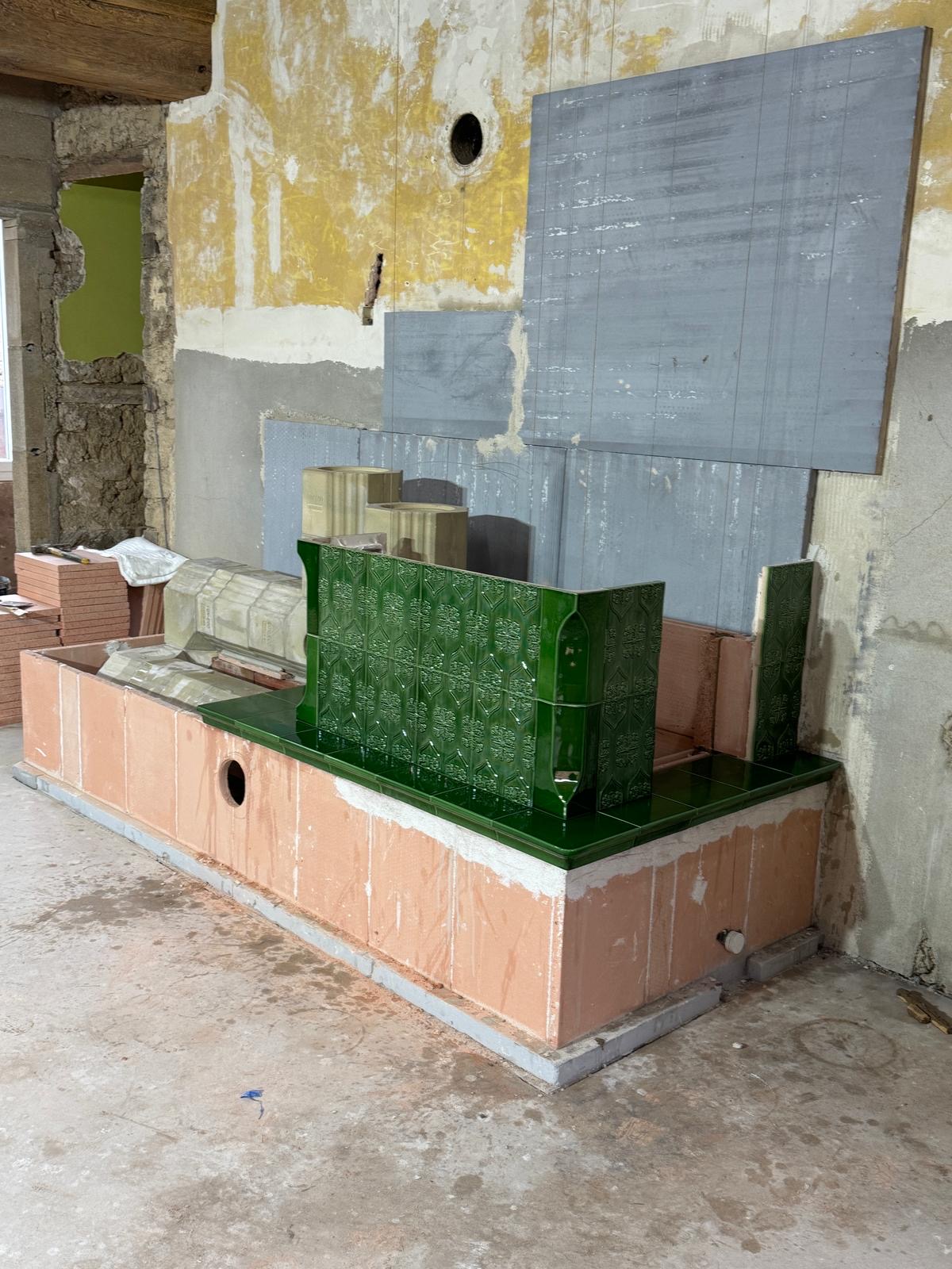Deep-green relief tiles being laid during the build on the site-built heated bench, in a room with stripped walls