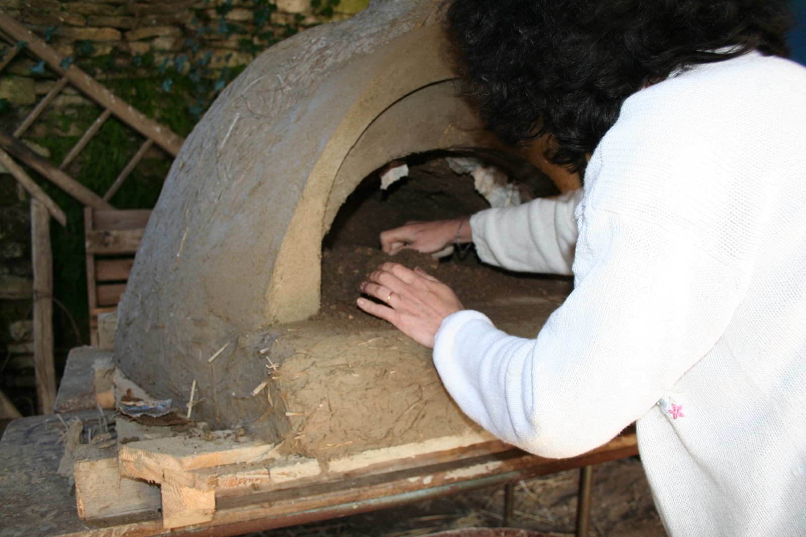 Hands smoothing the inside of the vault of a raw-earth oven being shaped