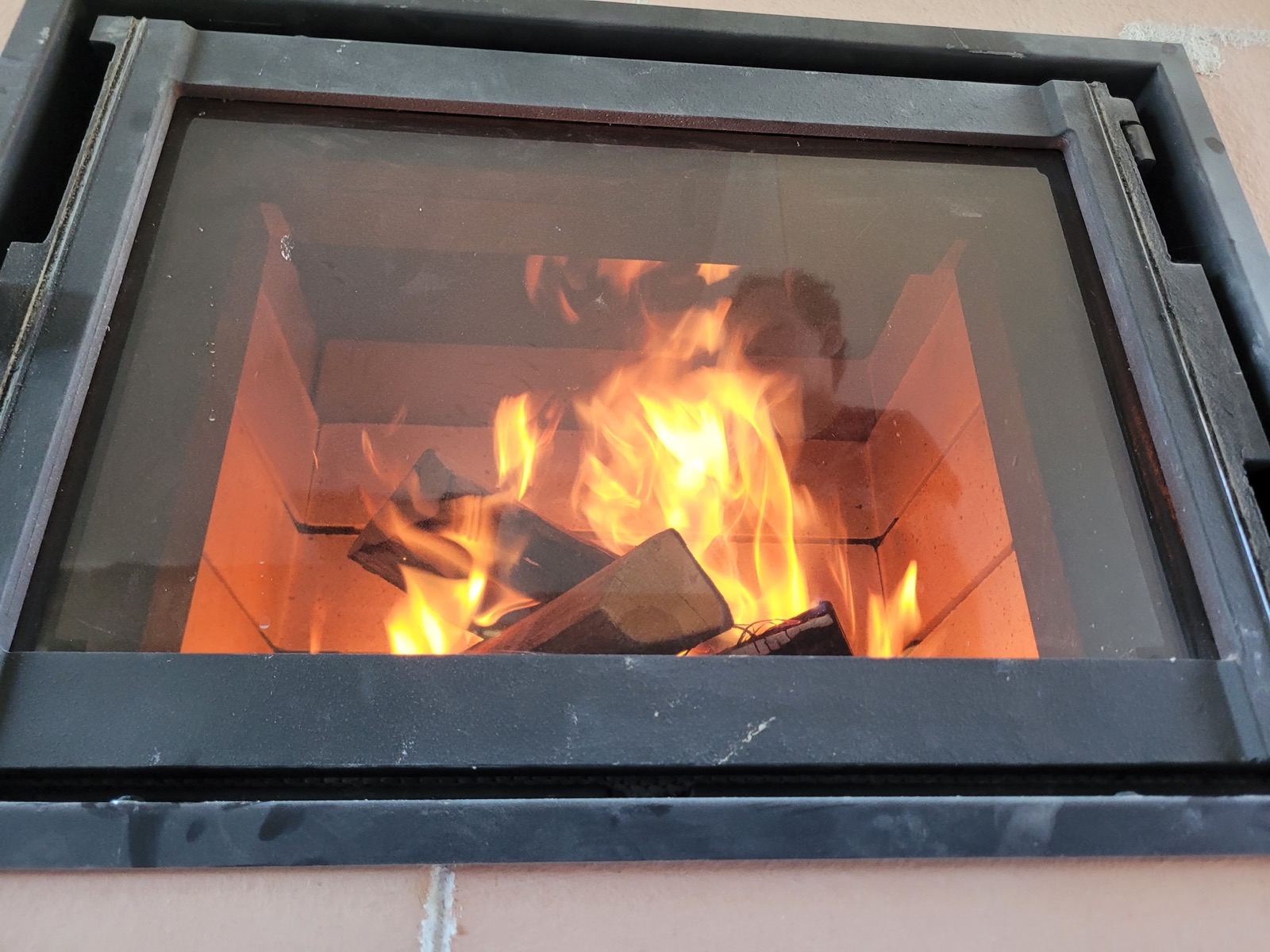 Close-up of the glazed firebox of a masonry heater in full burn, light-coloured firebricks visible at the back