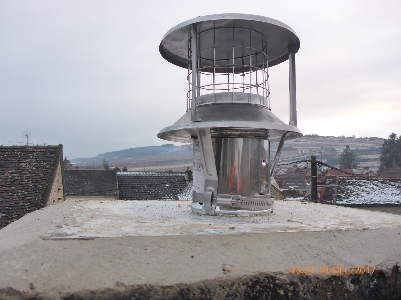 Stainless steel lined chimney stack with rain cap, on the snow-covered tiled roofs of a Burgundy village
