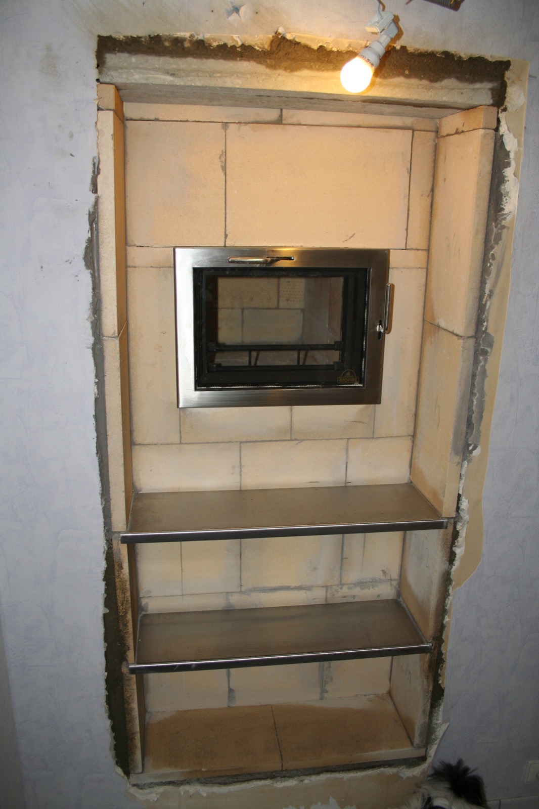 A heater recessed in its niche, above two stone shelves