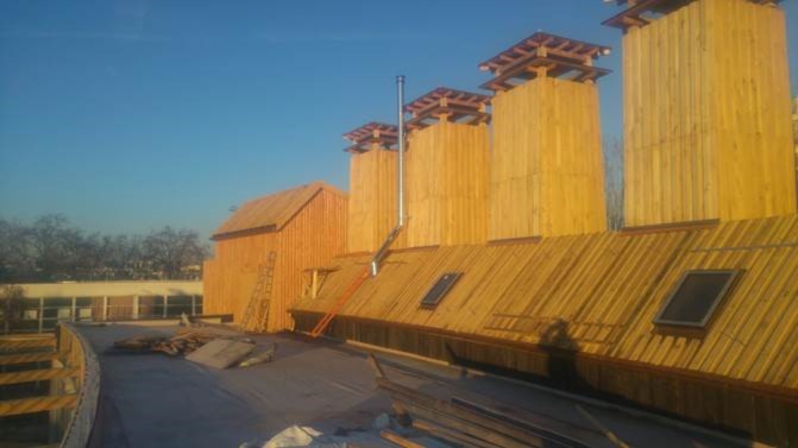 Roof of the building under construction: chimney stacks clad in vertical timber boarding, new structure and cladding, beneath a clear sky