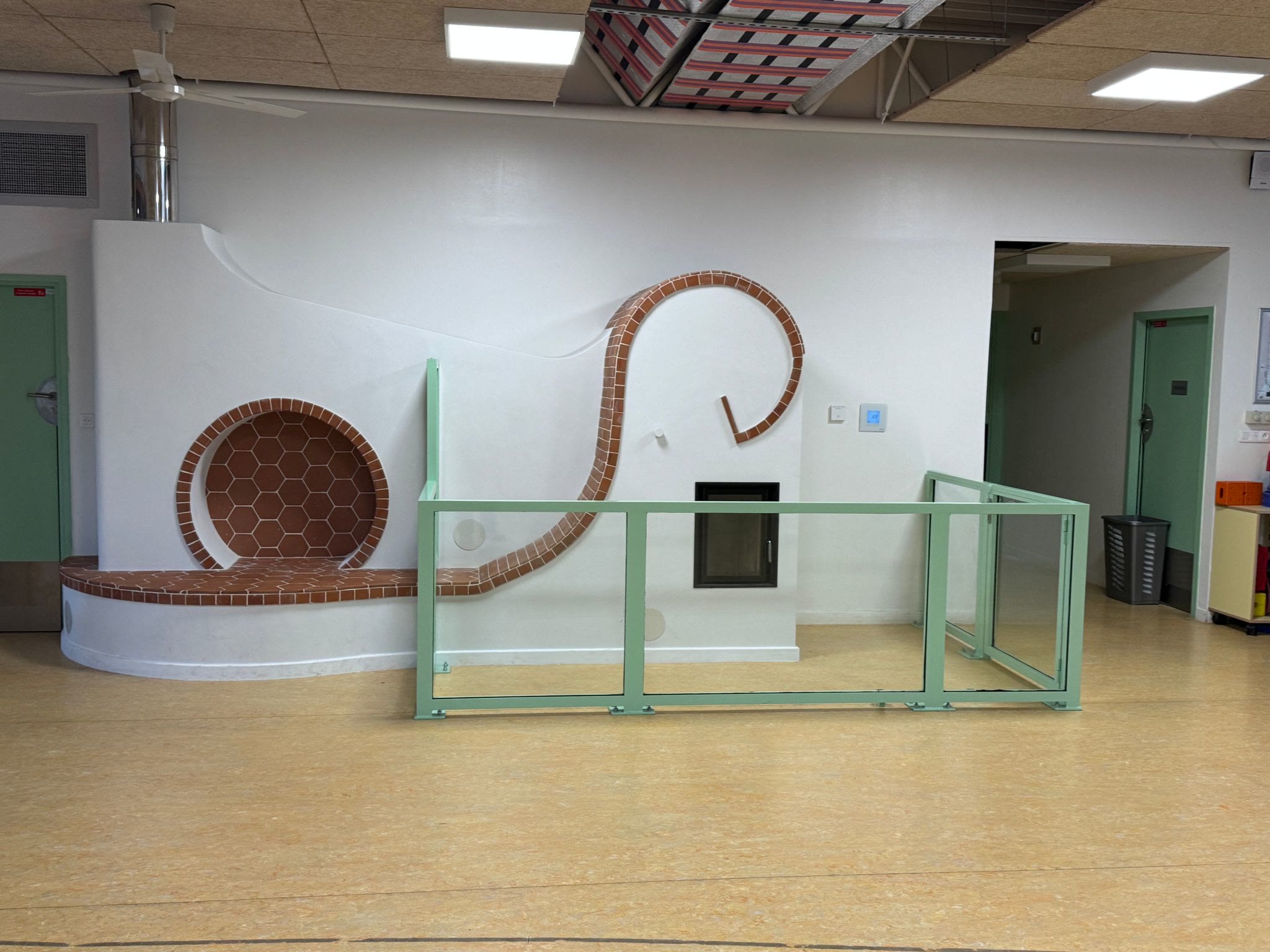The finished ‘snail’ heater seen from the front: terracotta spiral, round niche in hexagonal tiles and bench, behind its glass barrier