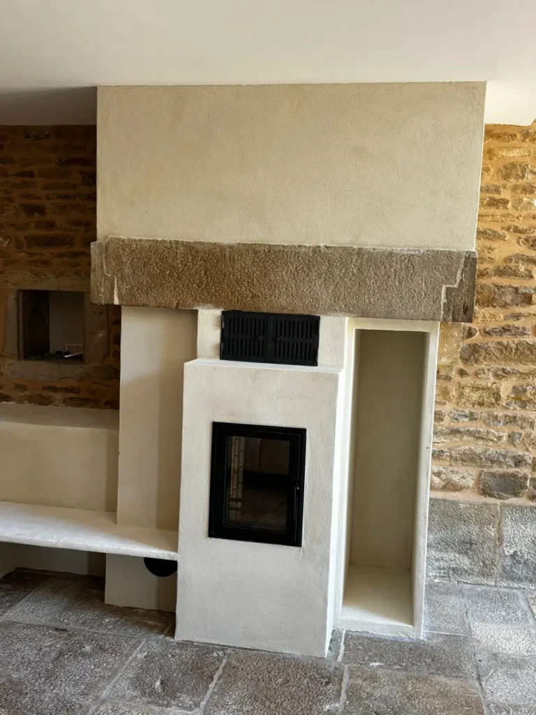 Front of the masonry heater: double-leaf grille of the plate-warmer, glazed firebox door and log niche beneath the stone lintel