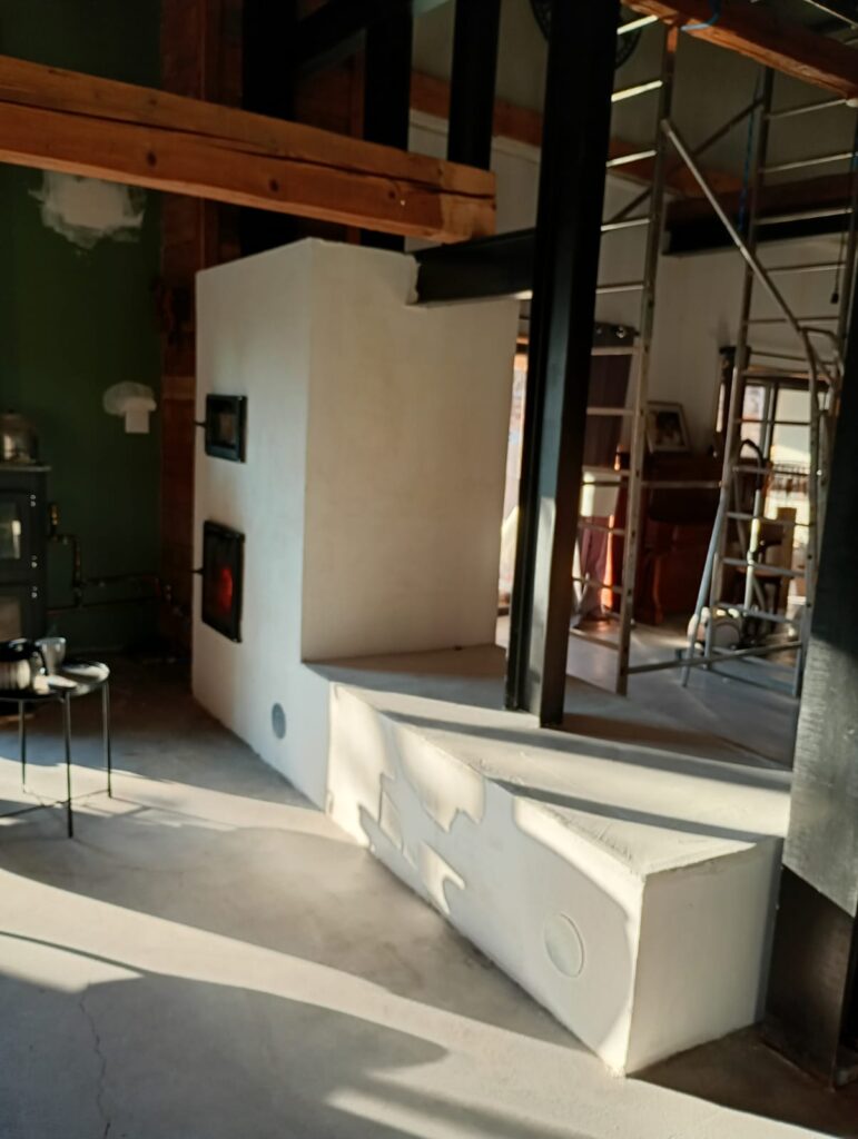 First fire in the finished masonry heater, light render and long heated bench, low-angled light
