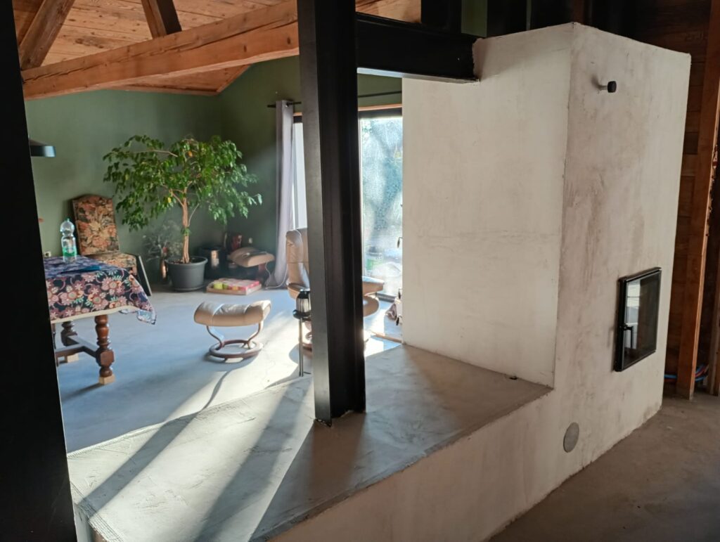The finished masonry heater seen from the living room, light-rendered mass and masonry seat
